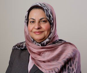 a woman wearing a pink scarf and a suit is smiling for the camera .