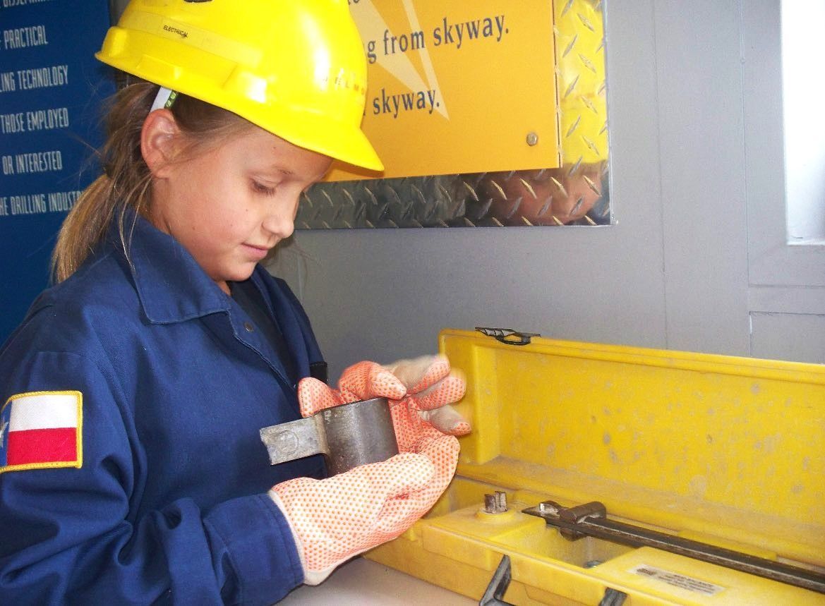 A young girl wearing a hard hat is holding a piece of metal