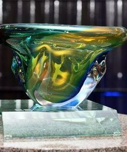 A green and yellow glass bowl is sitting on top of a glass base.
