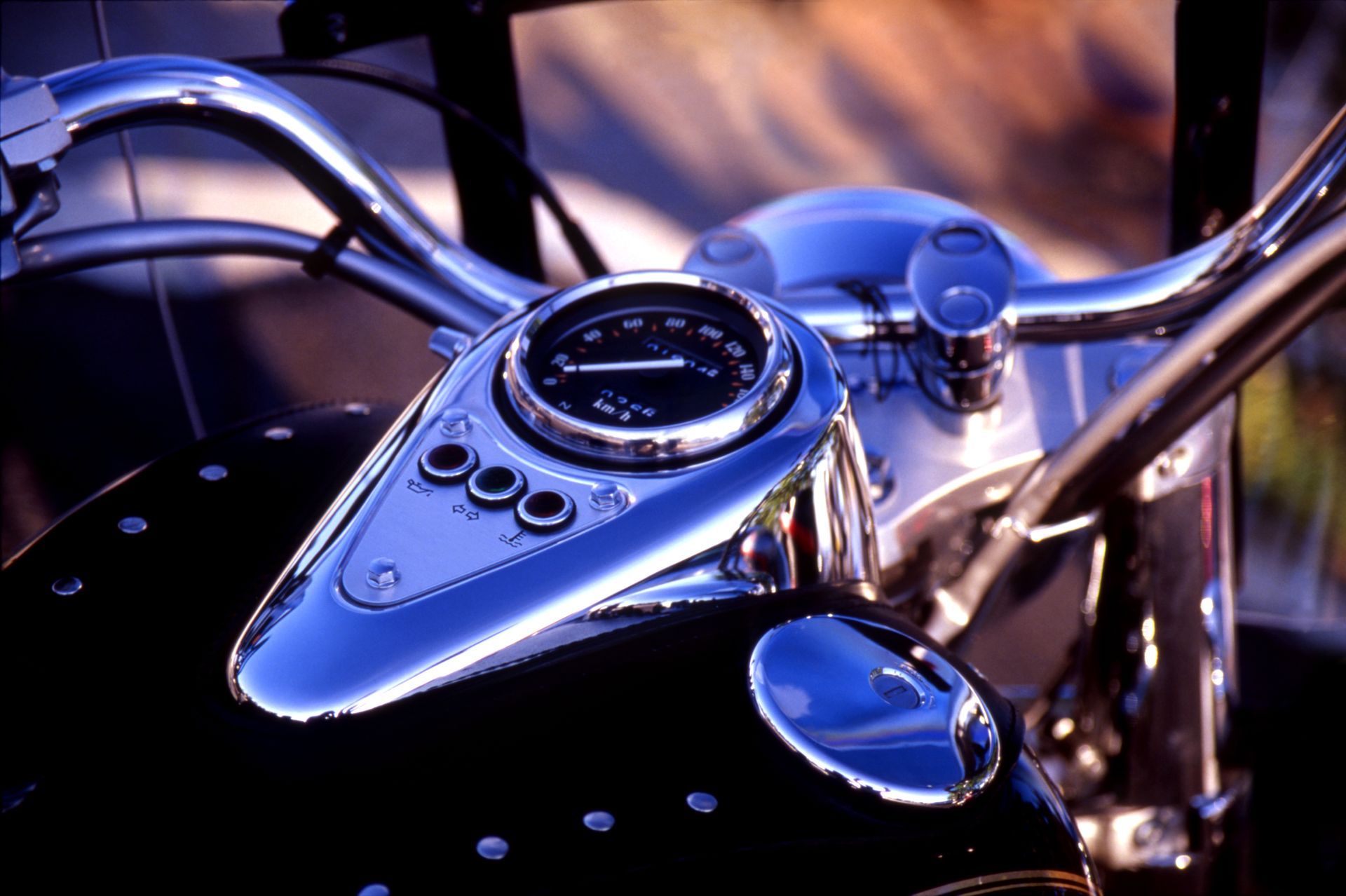Close-up of a motorcycle's chrome handlebar and instrument panel, including a speedometer and indicator lights.