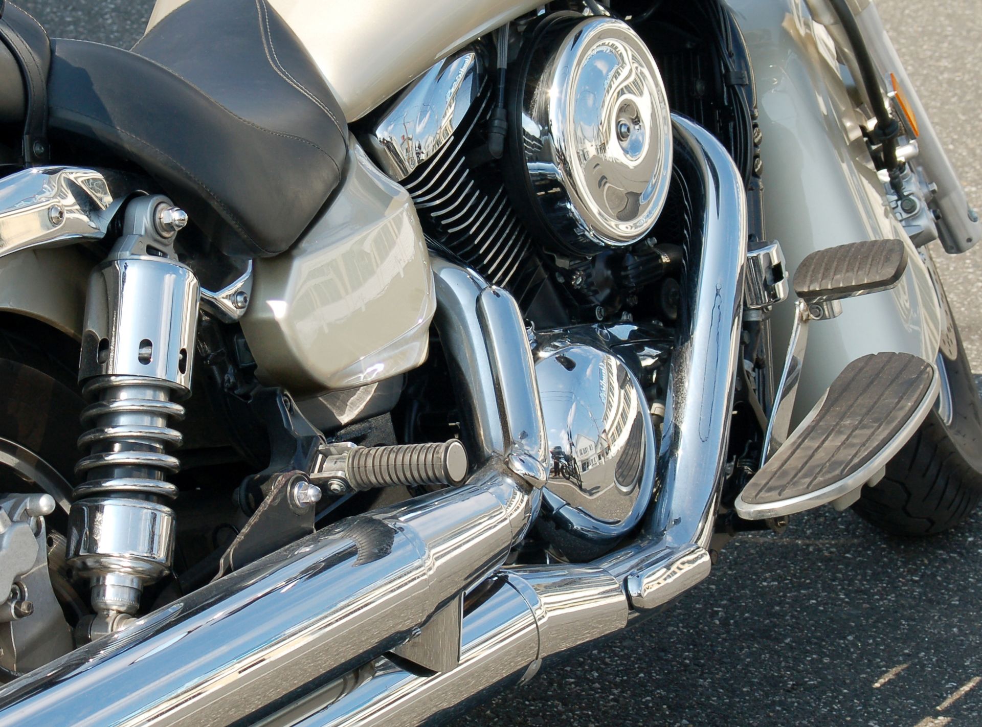 Close-up of a silver and chrome motorcycle engine and exhaust pipes, parked on asphalt.