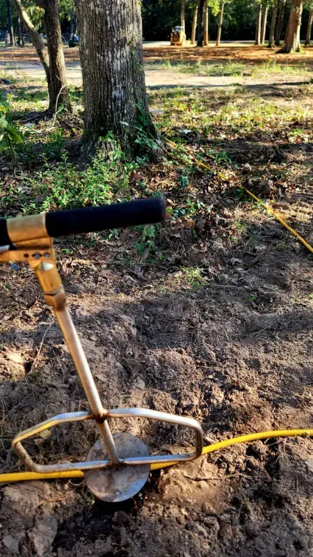 A metal detector is sitting in the dirt next to a tree.