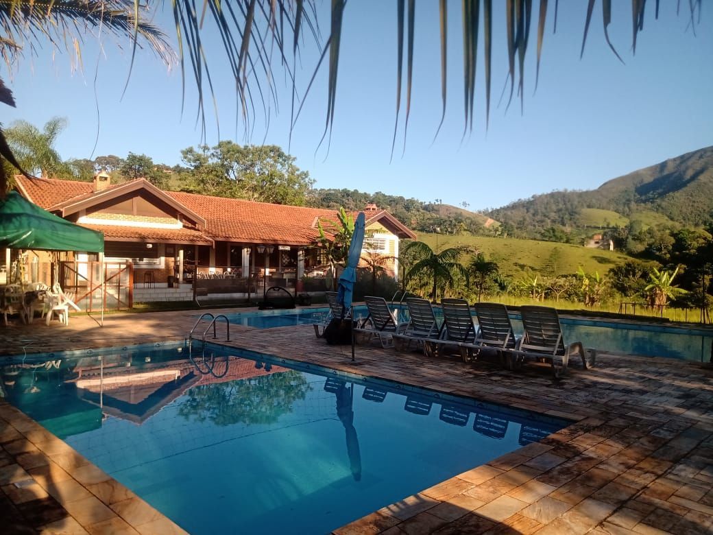 Piscina com casa e montanhas ao fundo. Água azul e um dia ensolarado.
