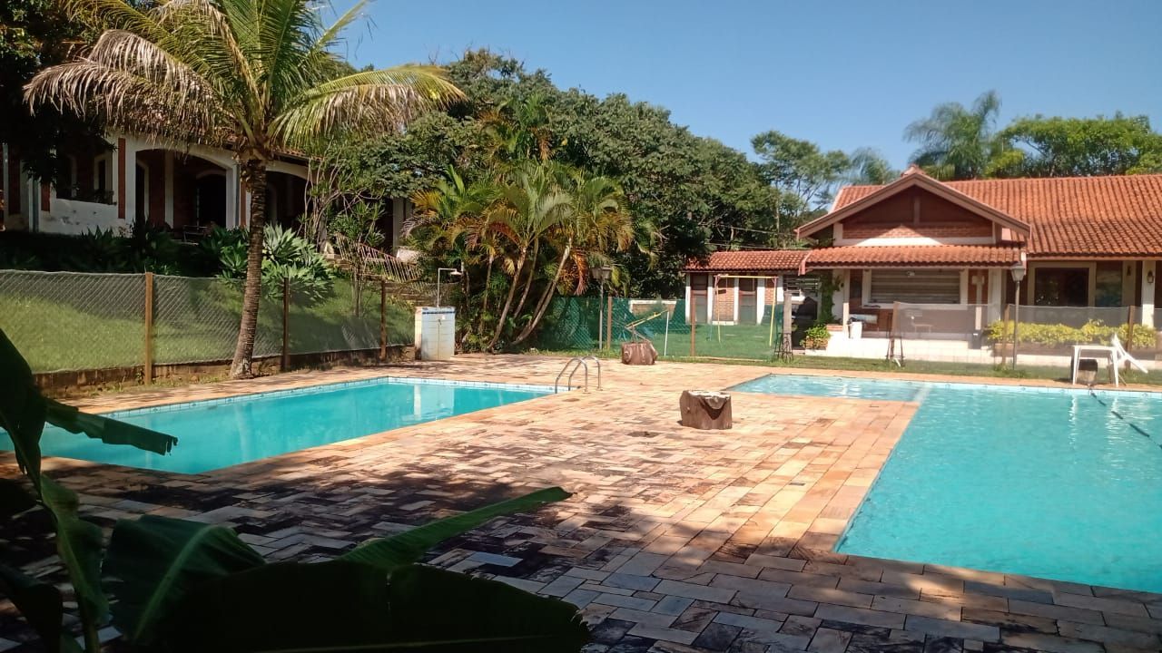 Duas piscinas com pátio de tijolos rodeadas por árvores e edifícios num dia ensolarado.