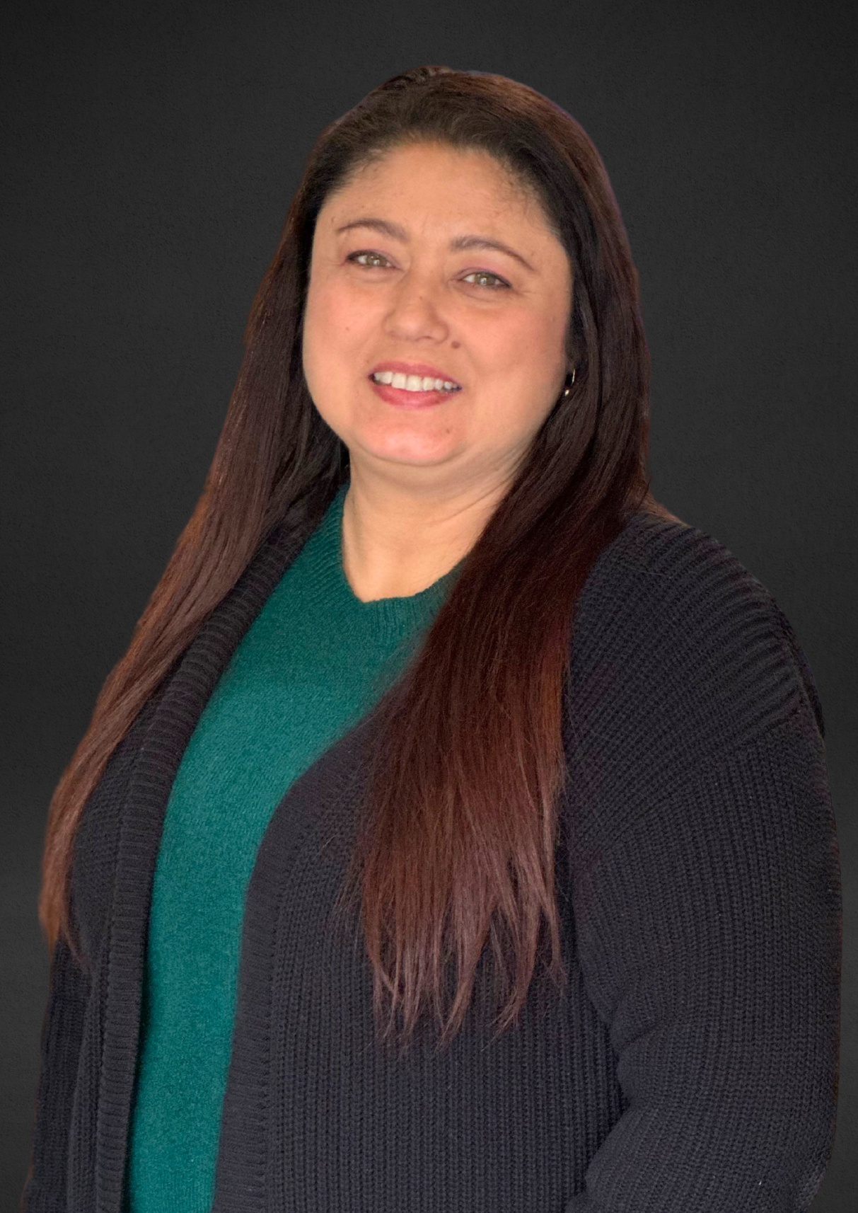 Woman smiling, wearing a green top and black cardigan, against a dark background.