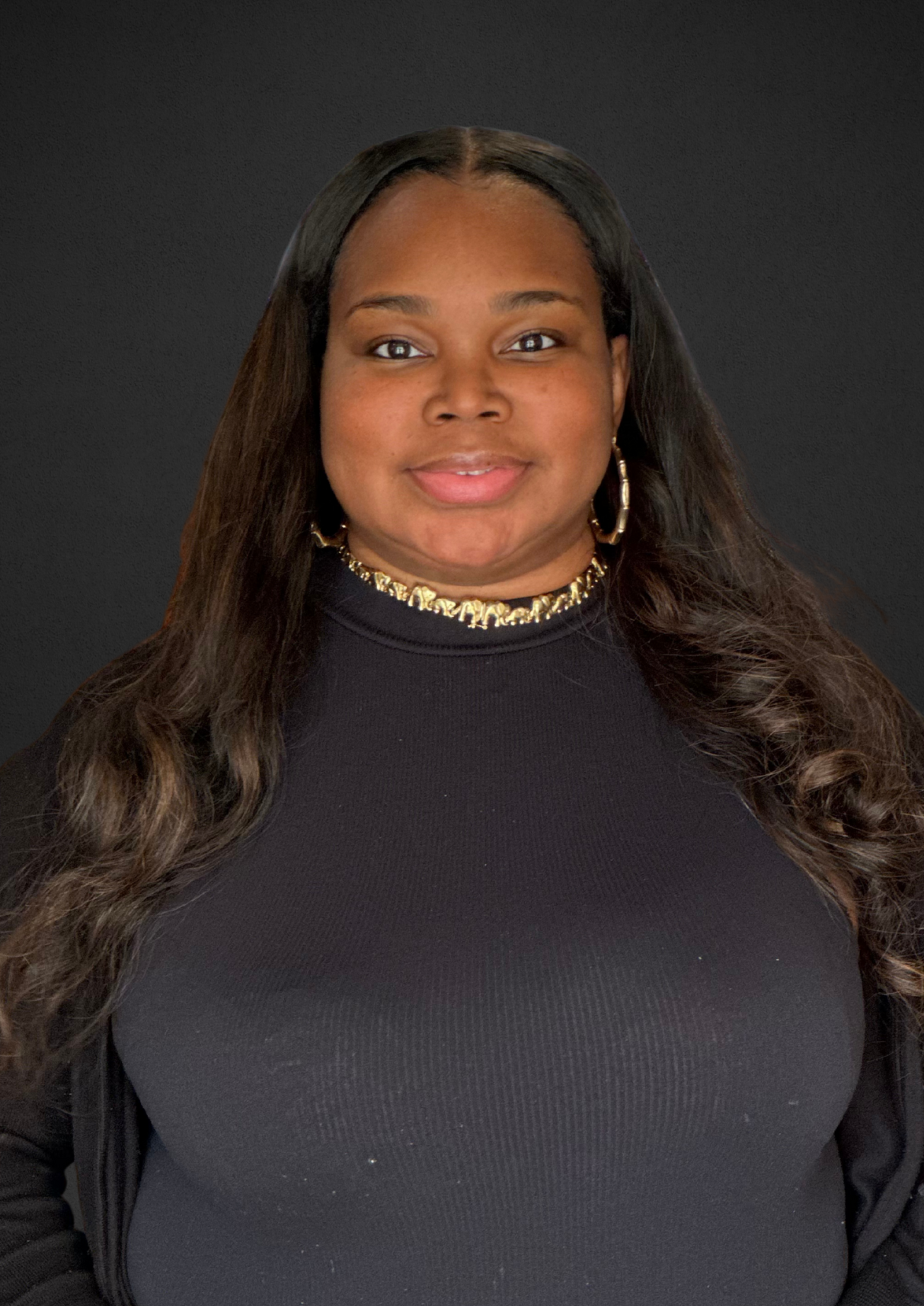 Woman with long dark hair, wearing a black top and gold necklace, smiles at the camera against a black background.