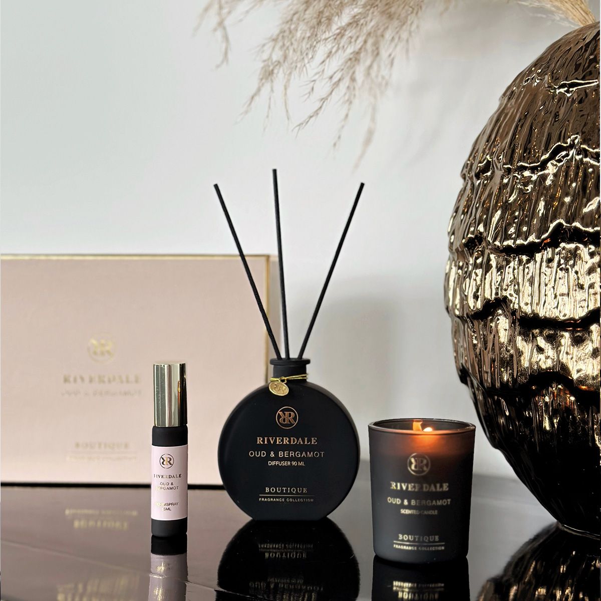 Roze geschenkdoos met zwarte geurstokjes, kaars en klein parfumflesje op een witte achtergrond.