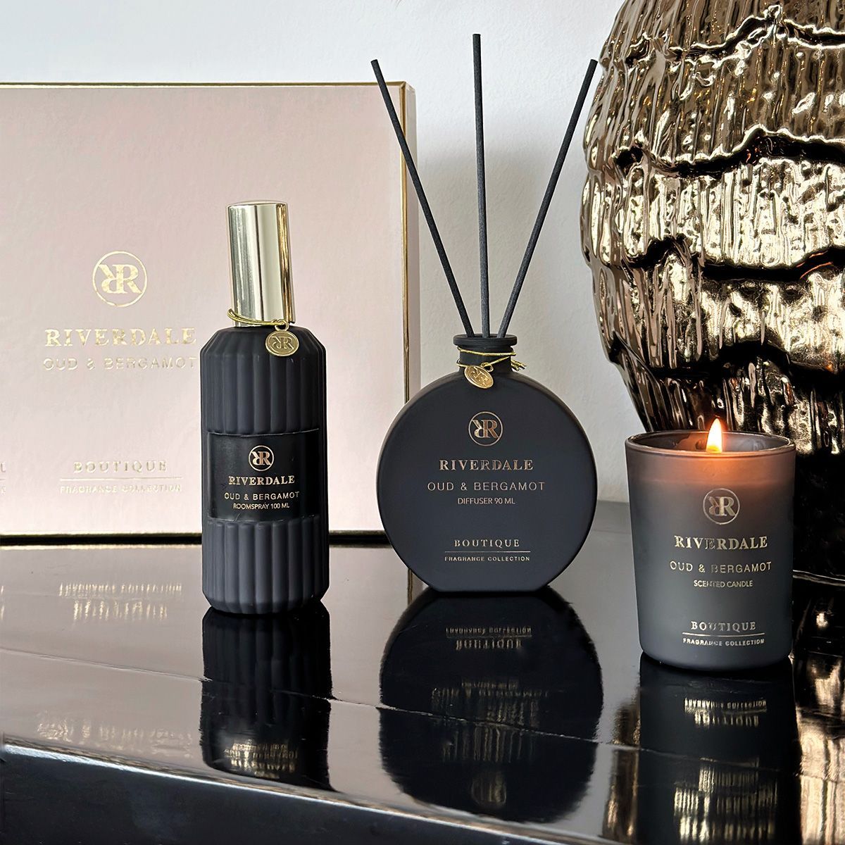 Roze geschenkdoos met drie zwarte geurstokjes en flesjes parfum op een witte achtergrond.