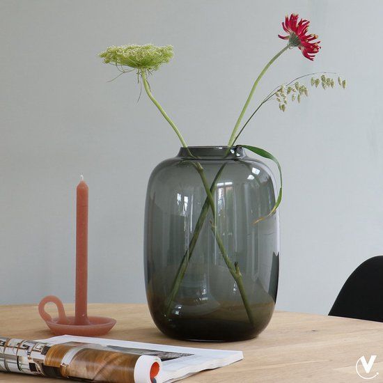 Een grijze vaas met bloemen en een kaars op een houten tafel.