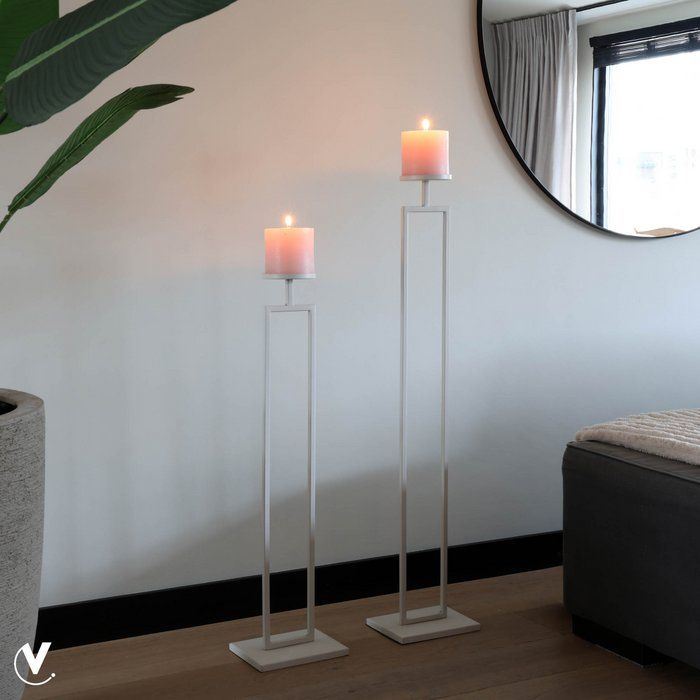 Hoge, wit metalen vloerkaarsenhouder met een donkergroene kaars.