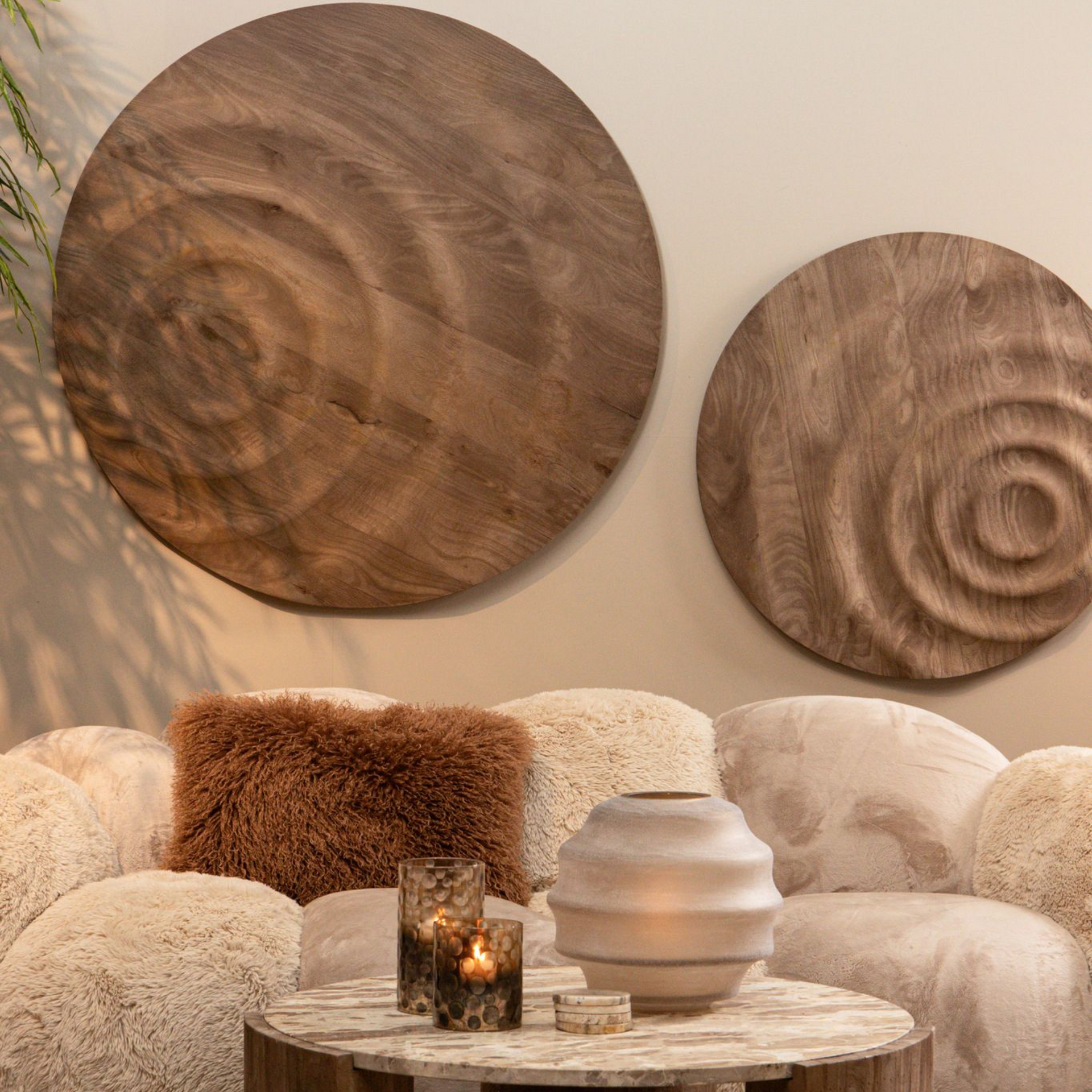 Houten wanddecoratie boven een bank met kussens en een salontafel met een vaas en kaarsen.