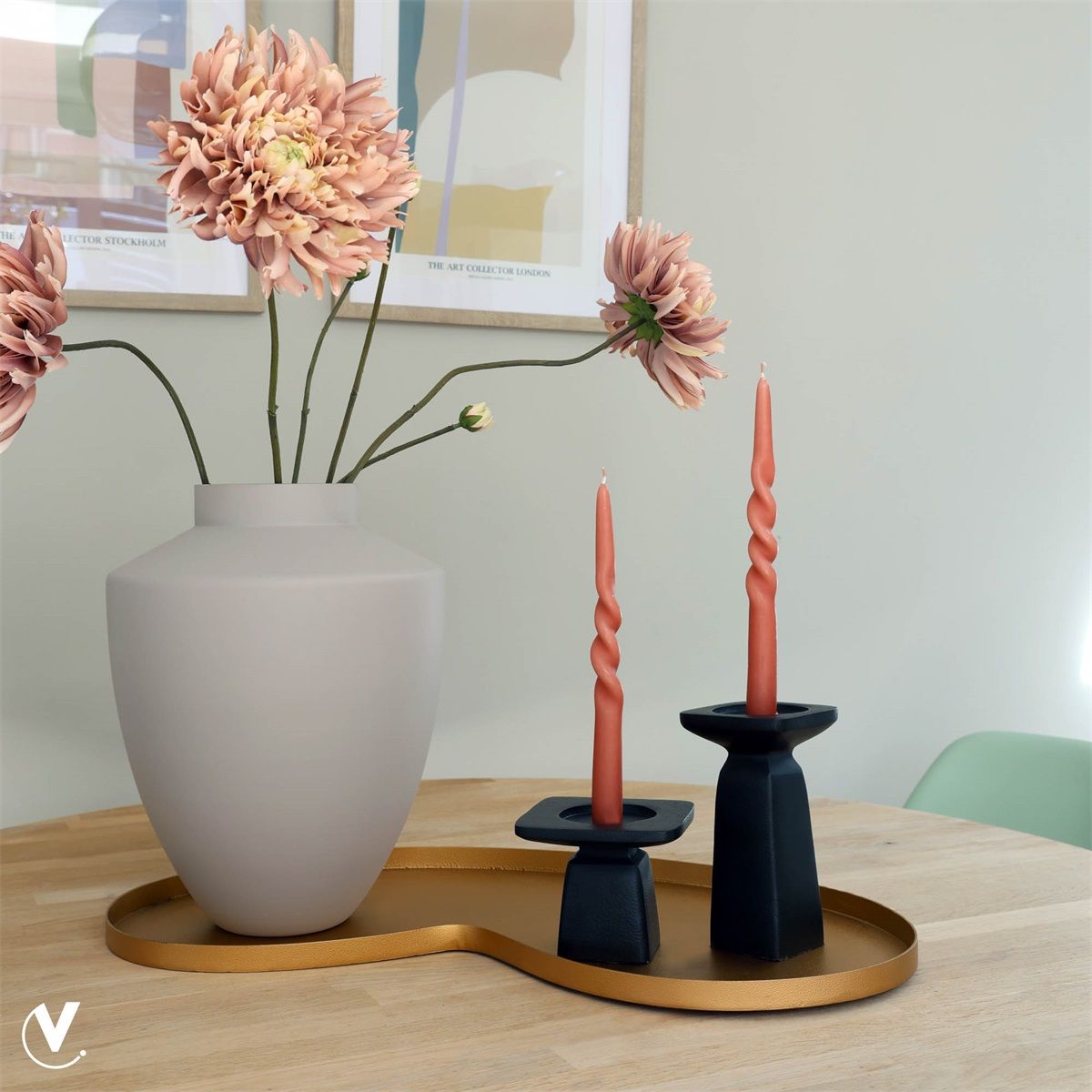 Een vaas met roze bloemen, twee spiraalvormige kaarsen in zwarte houders en een dienblad op een houten tafel.