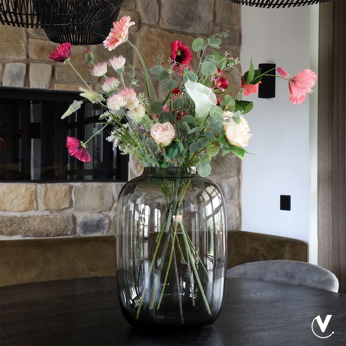 Een grijze vaas met bloemen en een kaars op een houten tafel.