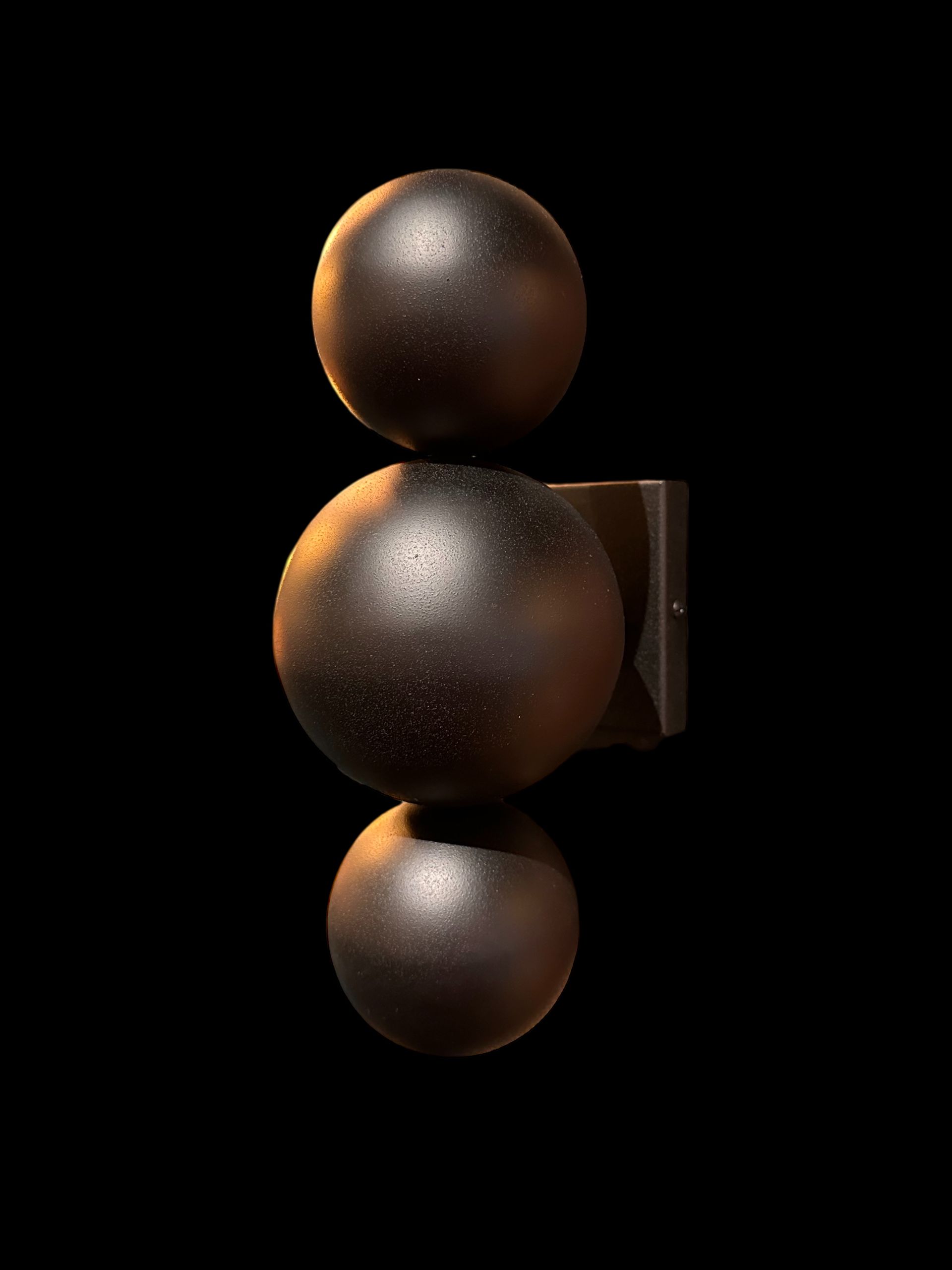 Zwartkleurige wandlamp met drie verticaal gestapelde bollen.