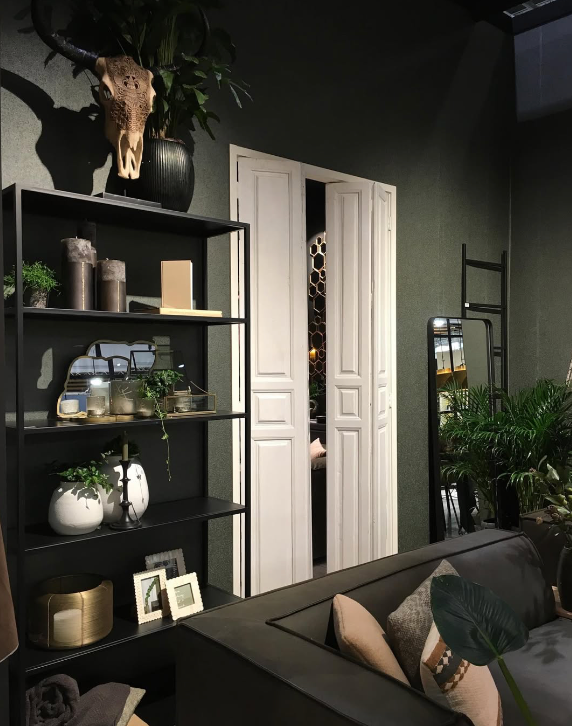 Stijlvolle woonkamer met zwarte planken, witte dubbele deuren, planten en een donkere bank met kussens.