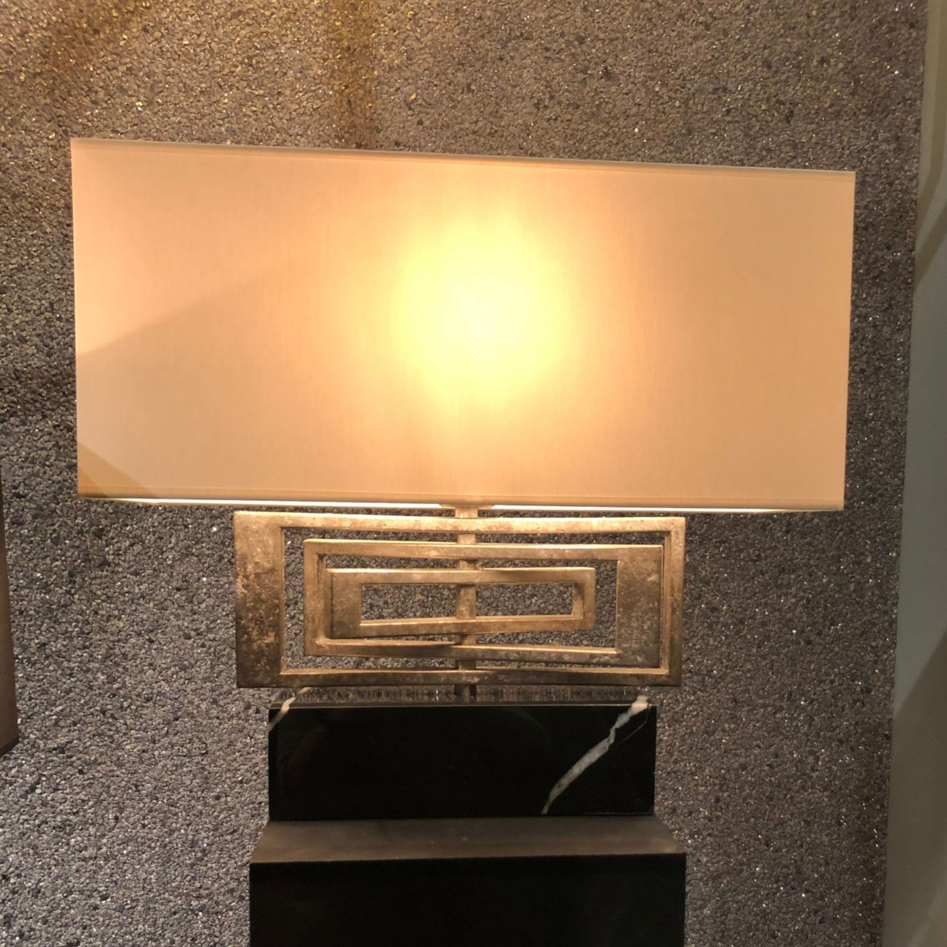Witte rechthoekige lamp met gouden details, op een zwarte marmeren voet.