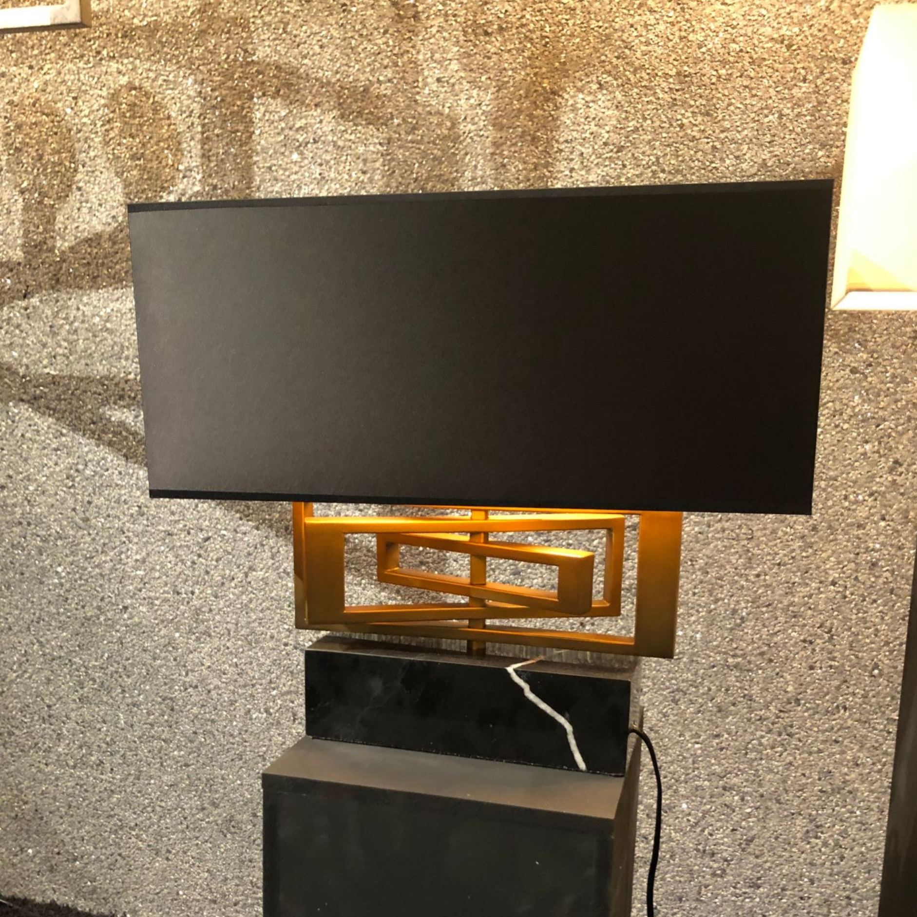 Zwarte rechthoekige lamp met gouden details, op een zwarte marmeren voet.
