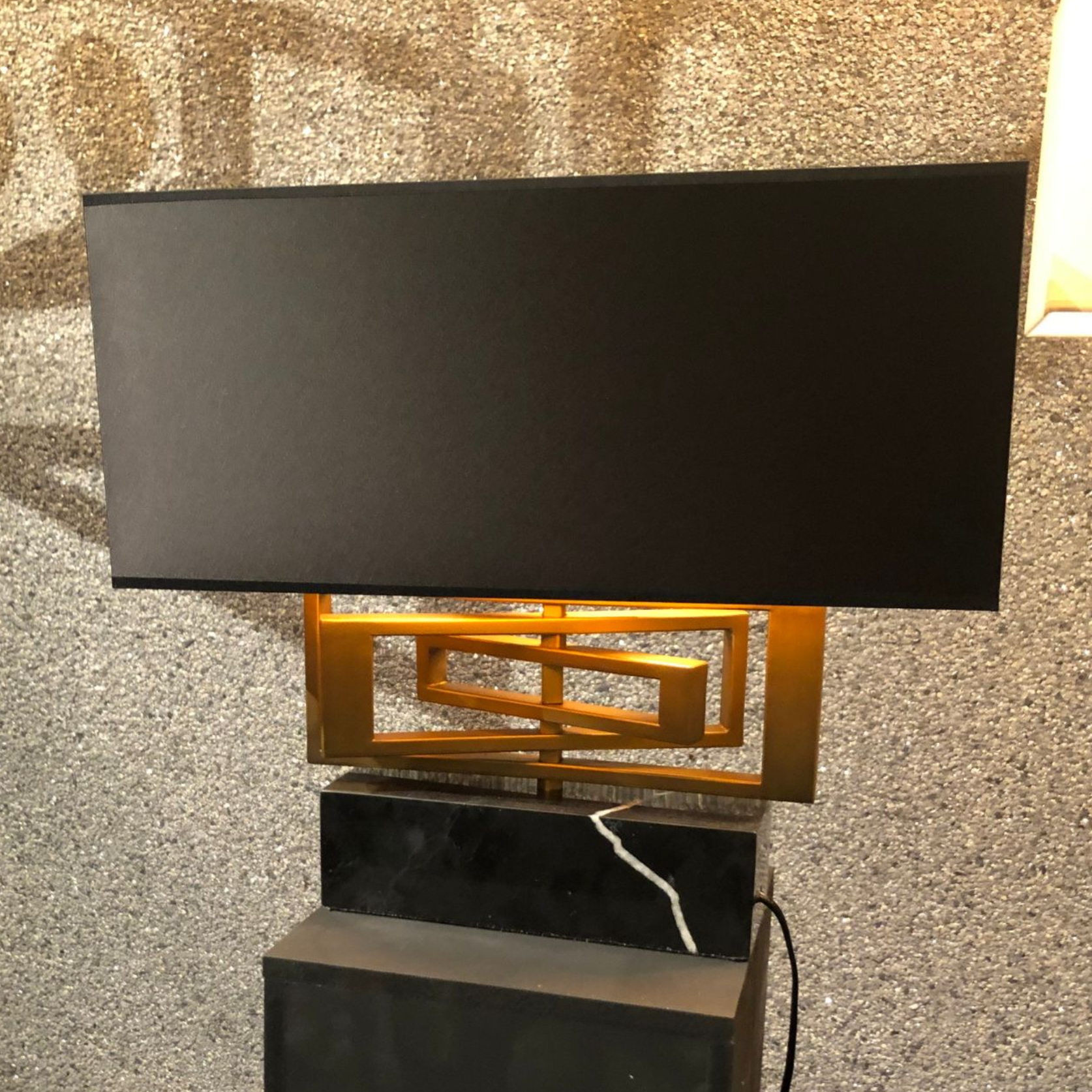 Zwarte rechthoekige lamp met gouden details, op een zwarte marmeren voet.