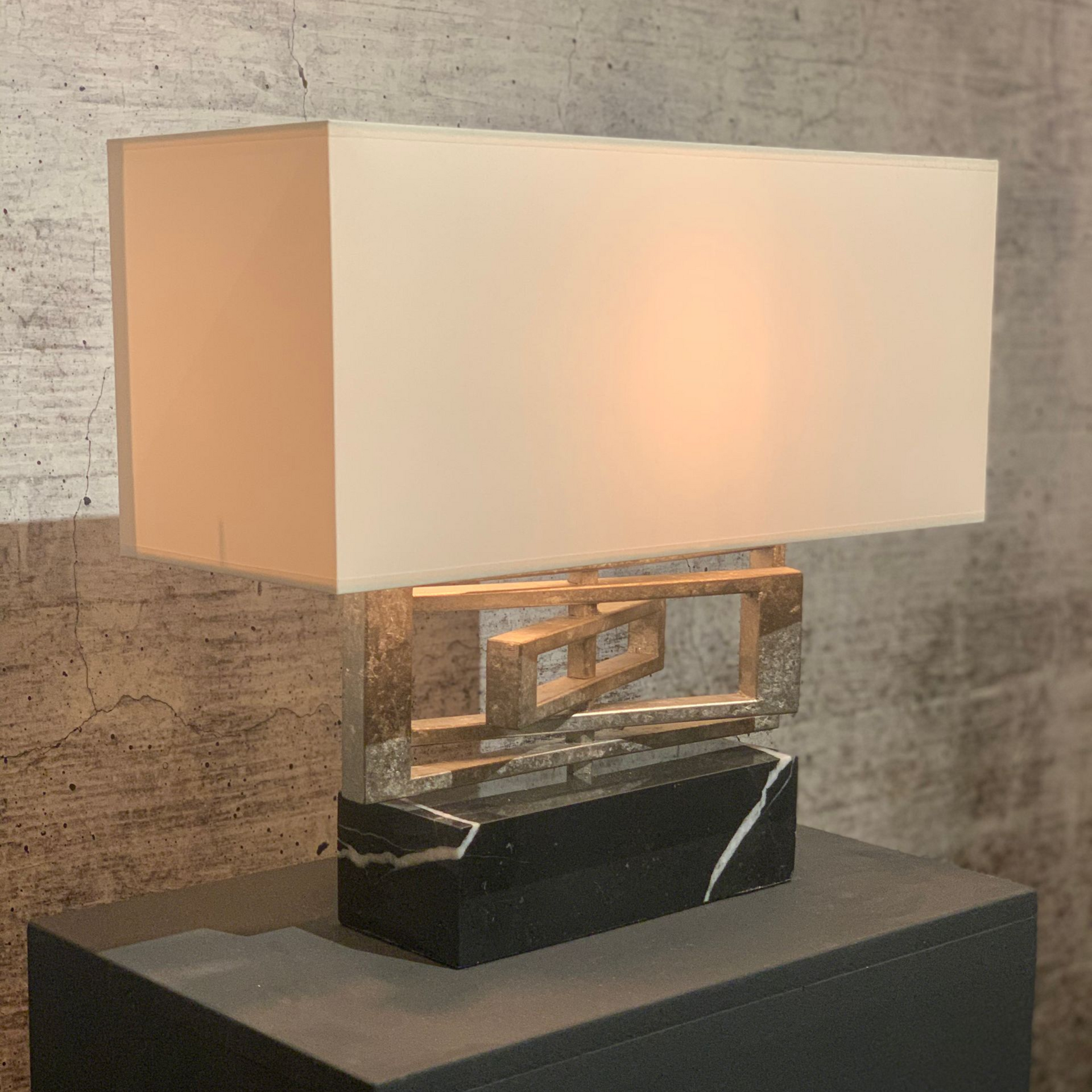 Witte rechthoekige lamp met gouden details, op een zwarte marmeren voet.