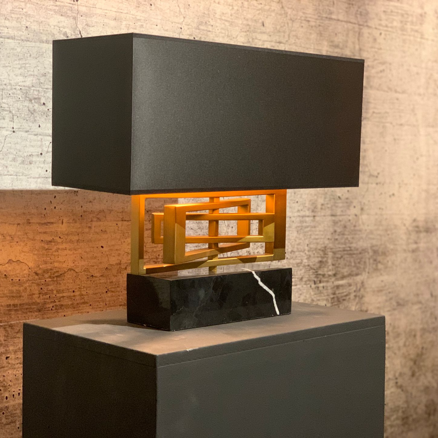 Zwarte rechthoekige lamp met gouden details, op een zwarte marmeren voet.