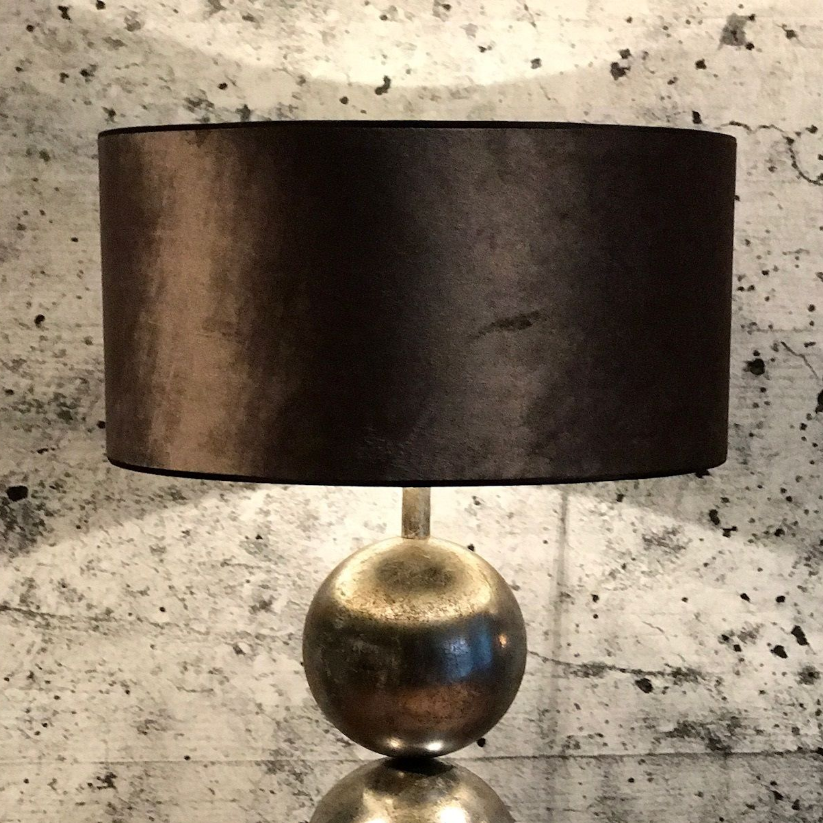 Een tafellamp met een cilindrische, donkerbruine kap, rustend op een gepolijste, verweerde metalen bolvormige voet.