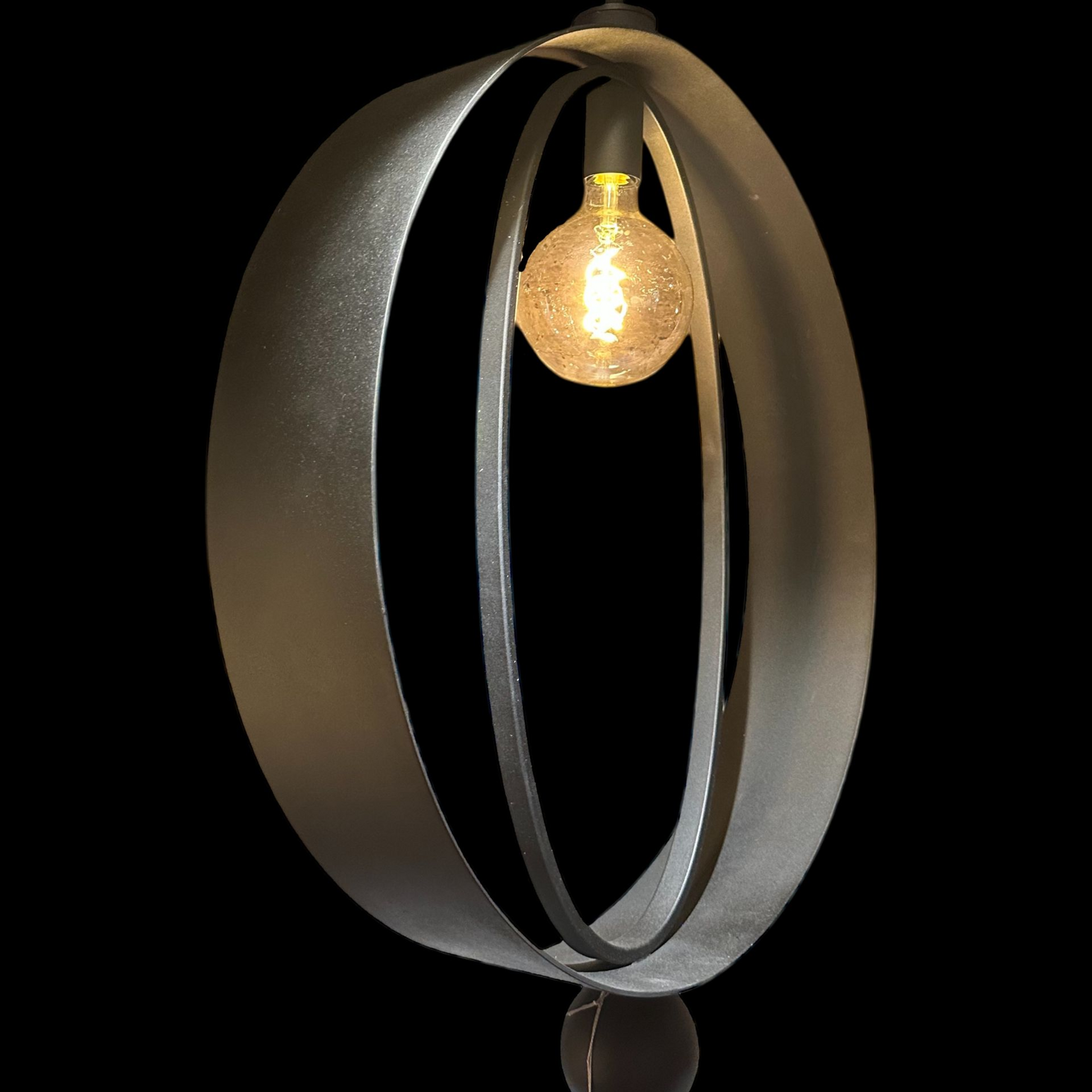 Een moderne tafellamp met een gloeilamp die is opgehangen in twee elkaar kruisende, zilverkleurige metalen ringen.