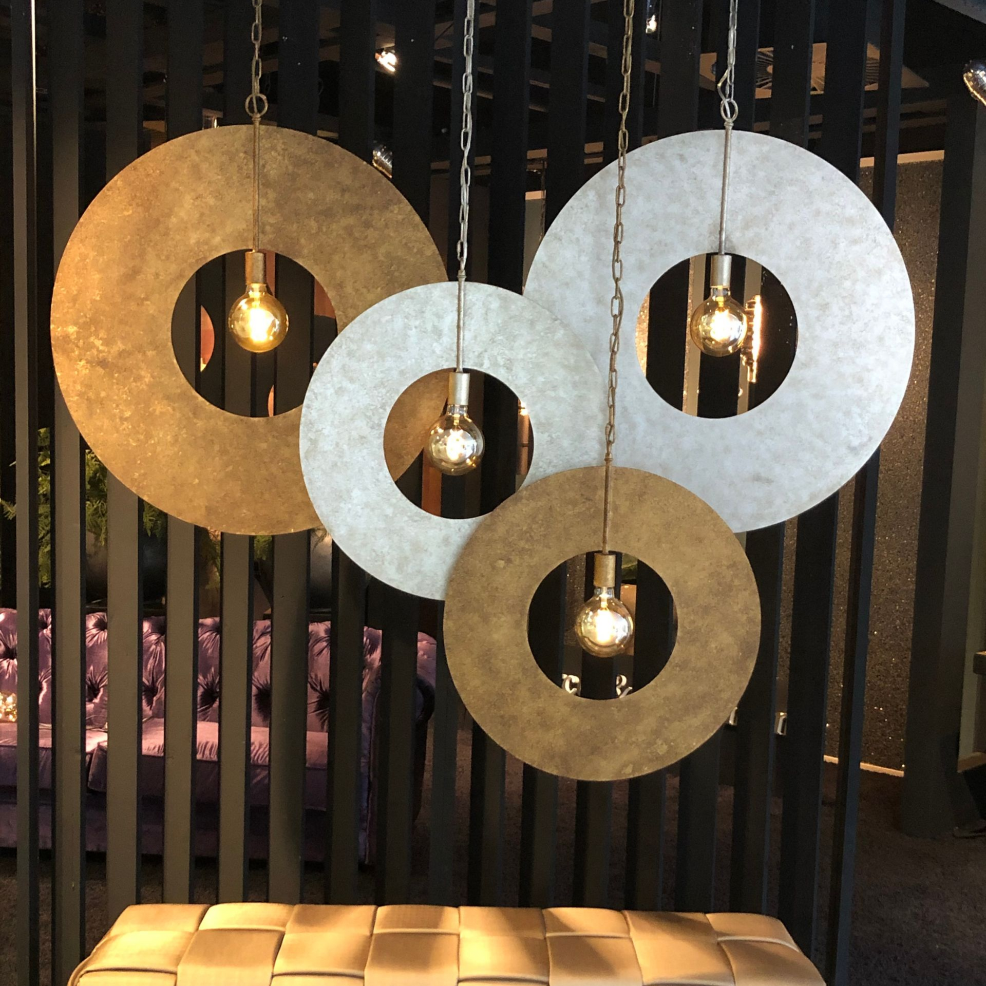 Vier ronde hanglampen met zichtbare lampen hangen voor een zwarte wand met lamellen.