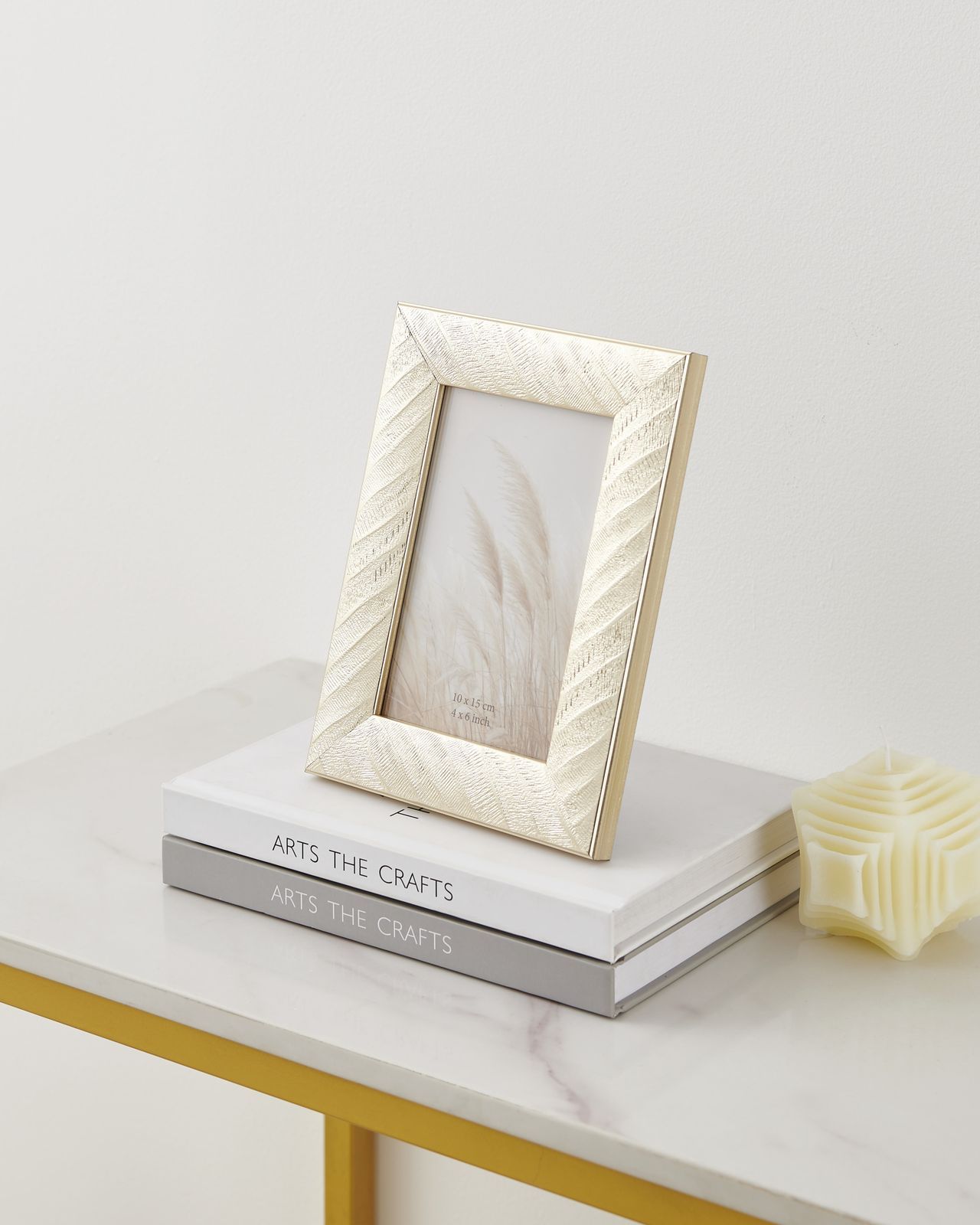 Gouden decoratieve fotolijst met een witte passe-partout en beige grasafbeelding, schuin gefotografeerd.