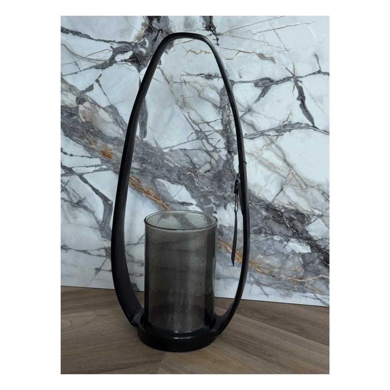 Zwarte metalen lantaarn met een grijze glazen cilinder voor een kaars.