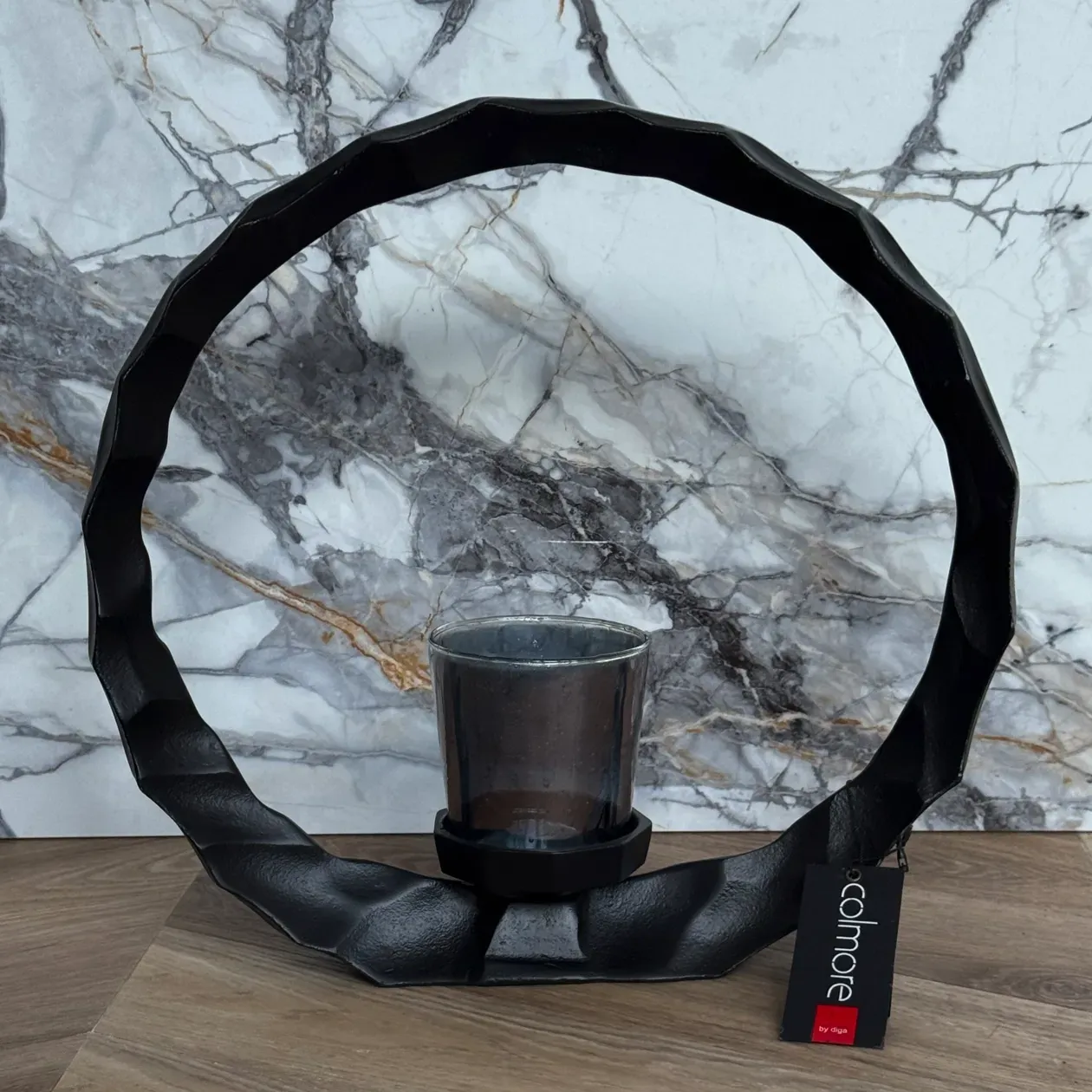 Zwarte ronde kaarsenhouder met een glazen votiefkaars in het midden.