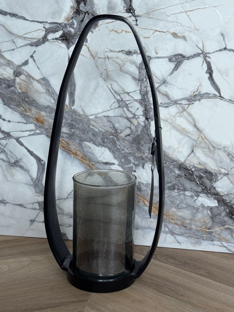 Zwarte metalen lantaarn met een grijze glazen cilinder voor een kaars.