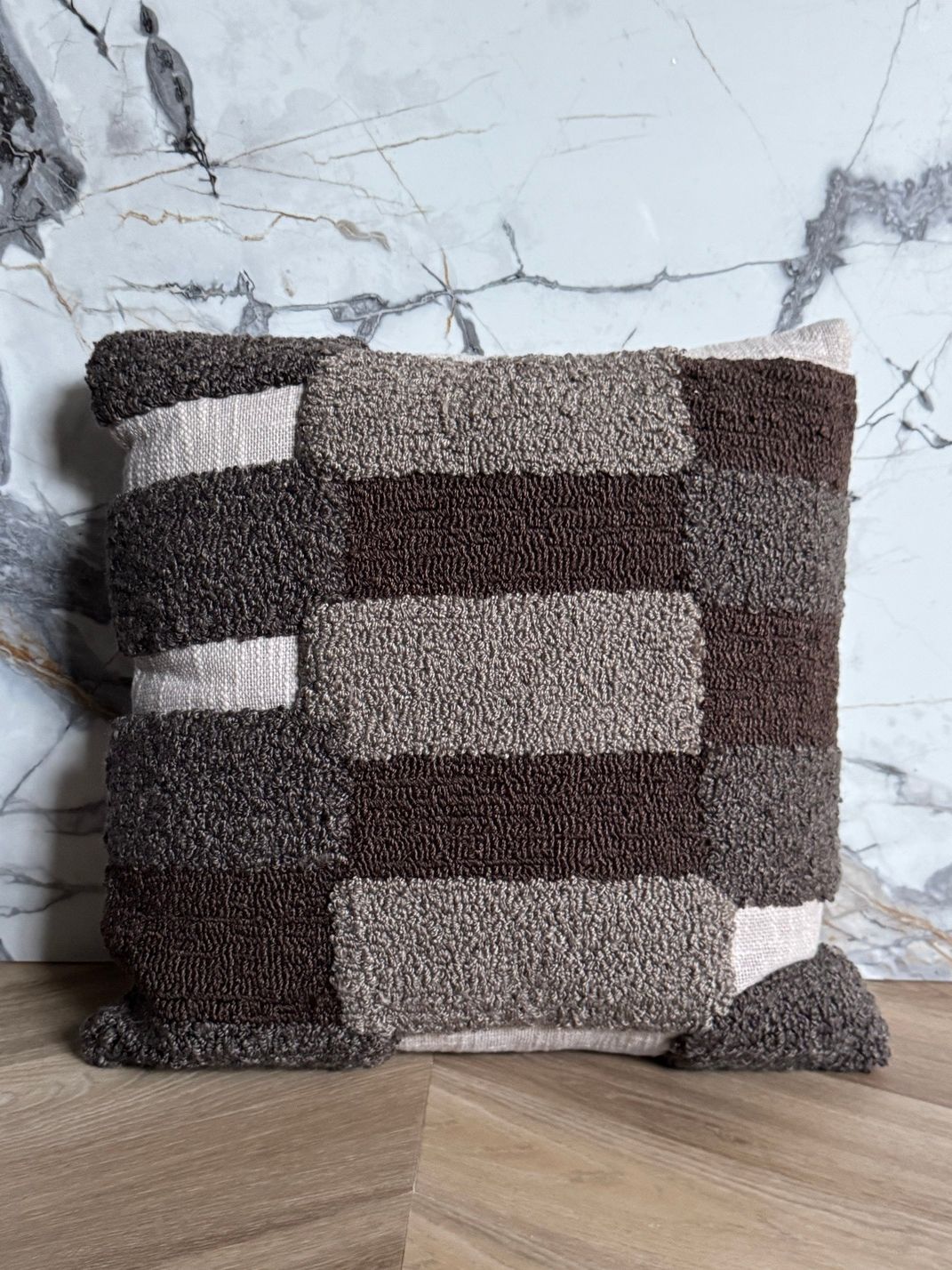 Vierkant kussen met een dambordpatroon van bruine en grijze, getufte blokken.
