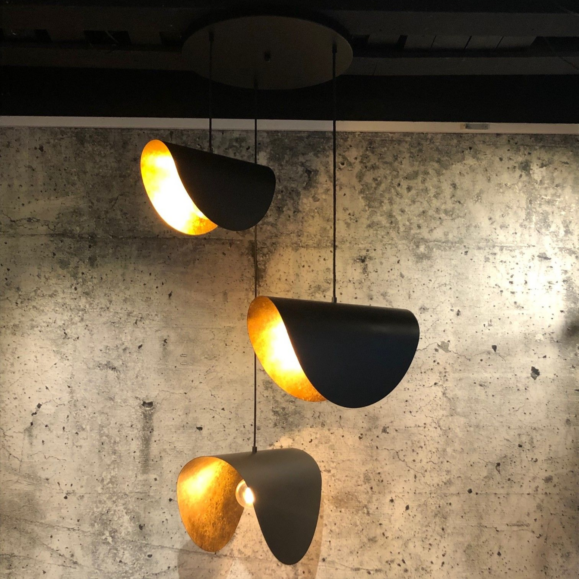 Zwarte hanglamp met gouden binnenkant, hangend tegen een grijze muur met structuur.