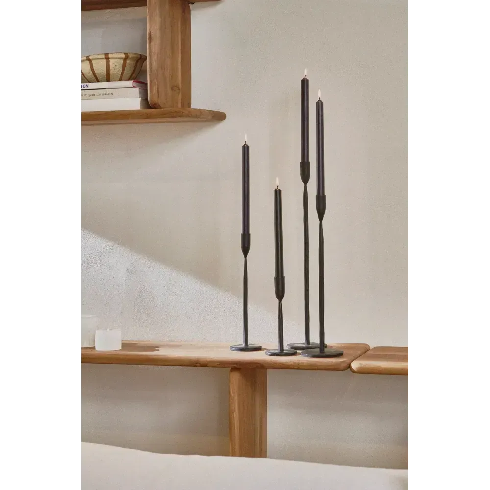 Zwarte kandelaars op een houten plank naast een klein, aan de muur bevestigd houten kastje.