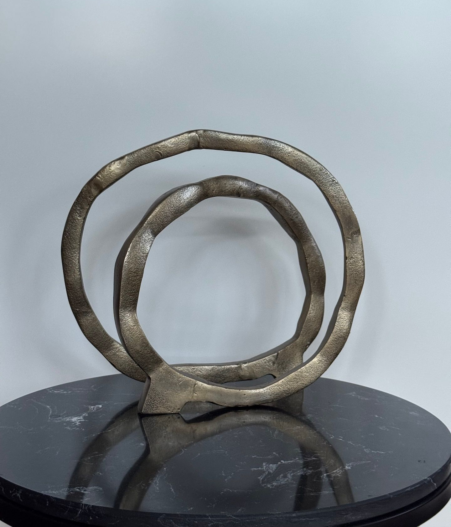 Abstracte gouden metalen sculptuur bestaande uit twee met elkaar verbonden ringen op een donker, rond oppervlak.