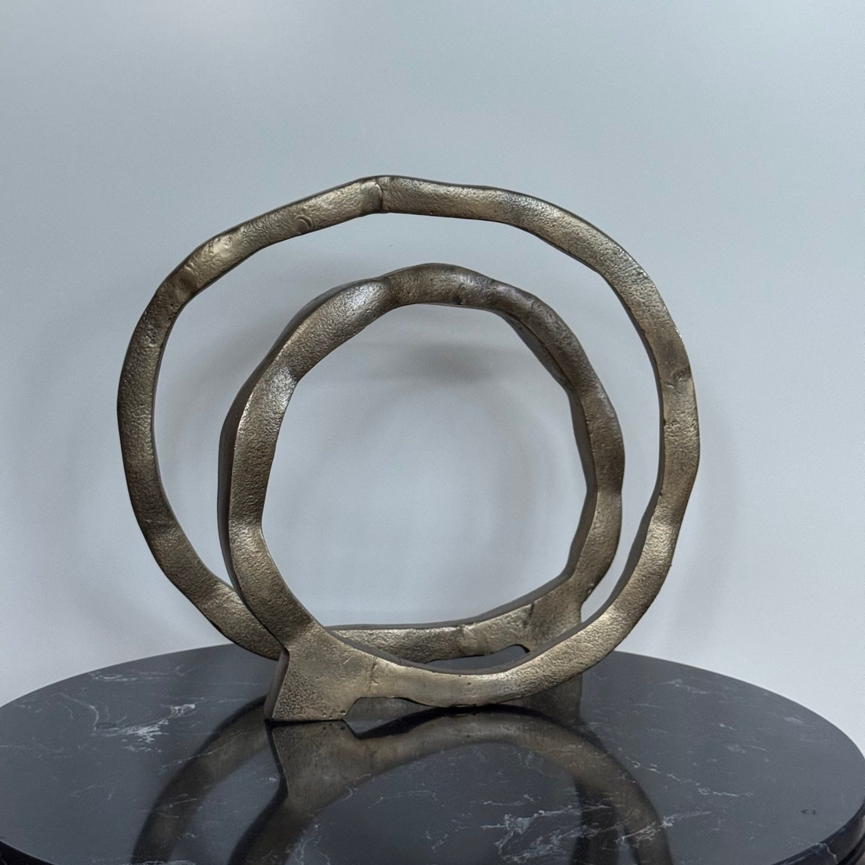 Abstracte gouden metalen sculptuur bestaande uit twee met elkaar verbonden ringen op een donker, rond oppervlak.