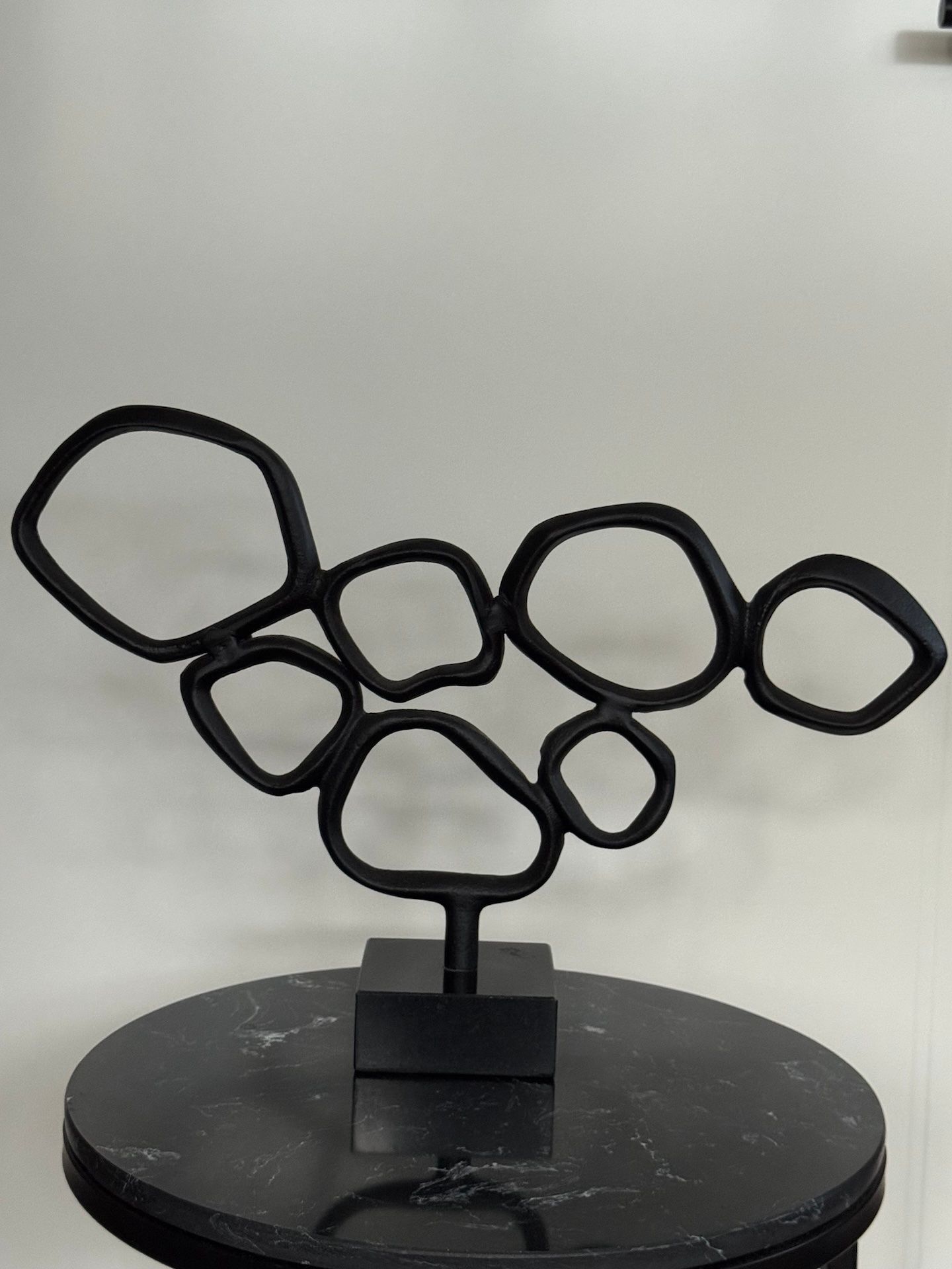 Abstracte sculptuur van zwart metaal op een zwarte marmeren ondergrond.