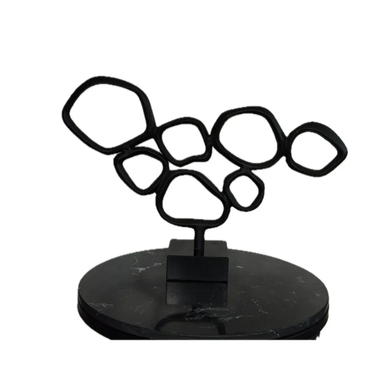 Een sculptuur van zwart metaal, bestaande uit met elkaar verbonden organische vormen, op een zwarte marmeren sokkel.