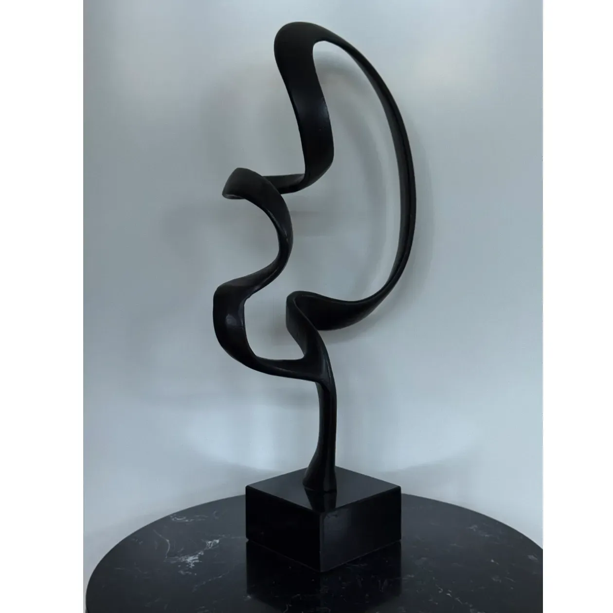 Zwarte abstracte sculptuur op een zwarte vierkante sokkel met een marmerachtig oppervlak.