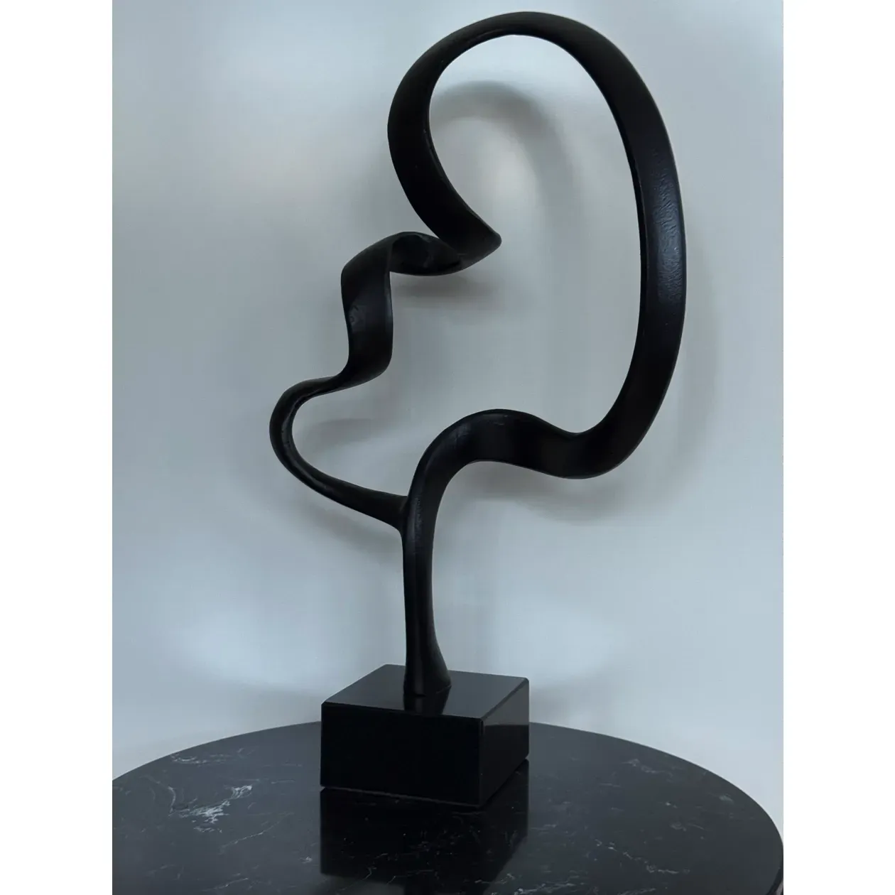 Zwarte abstracte sculptuur op een zwarte vierkante sokkel met een marmerachtig oppervlak.