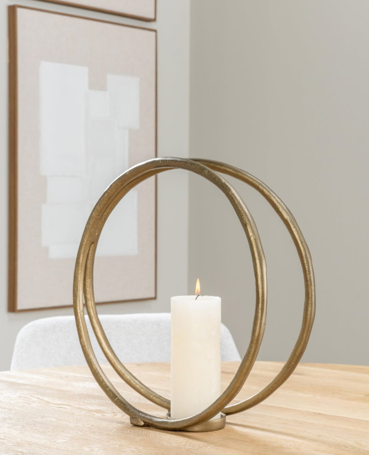 Gouden kandelaar met brandende witte kaars op een houten tafel, kunstwerk op de achtergrond.