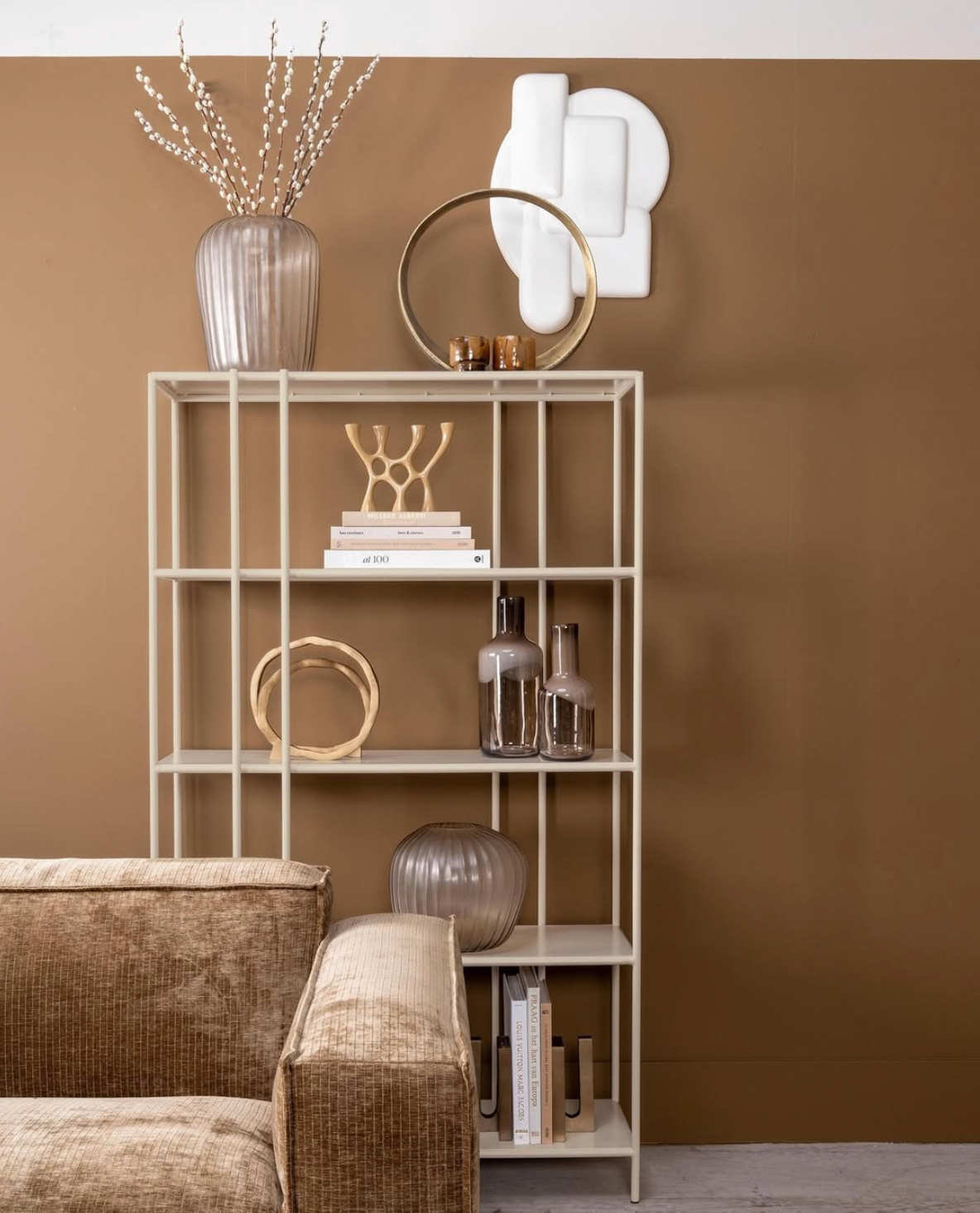 Beige bank met zwarte salontafel, decoratieve wanddecoratie en een raam met zwarte kozijnen.