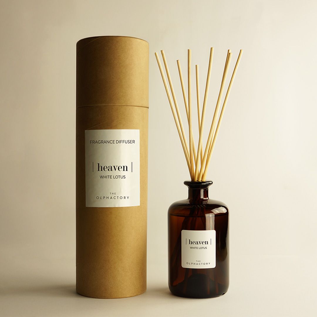 Twee amberkleurige rietdiffuserflessen met zwarte rietjes op een beige ondergrond, één ervoor en één erachter weerspiegeld.