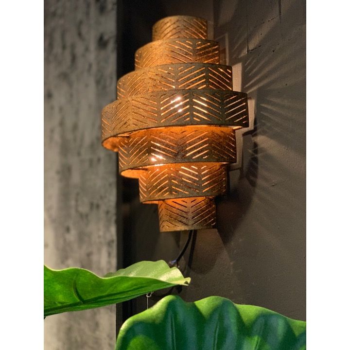 Gouden wandlamp met meerdere lagen en sierlijke uitsparingen, die warm licht uitstraalt.