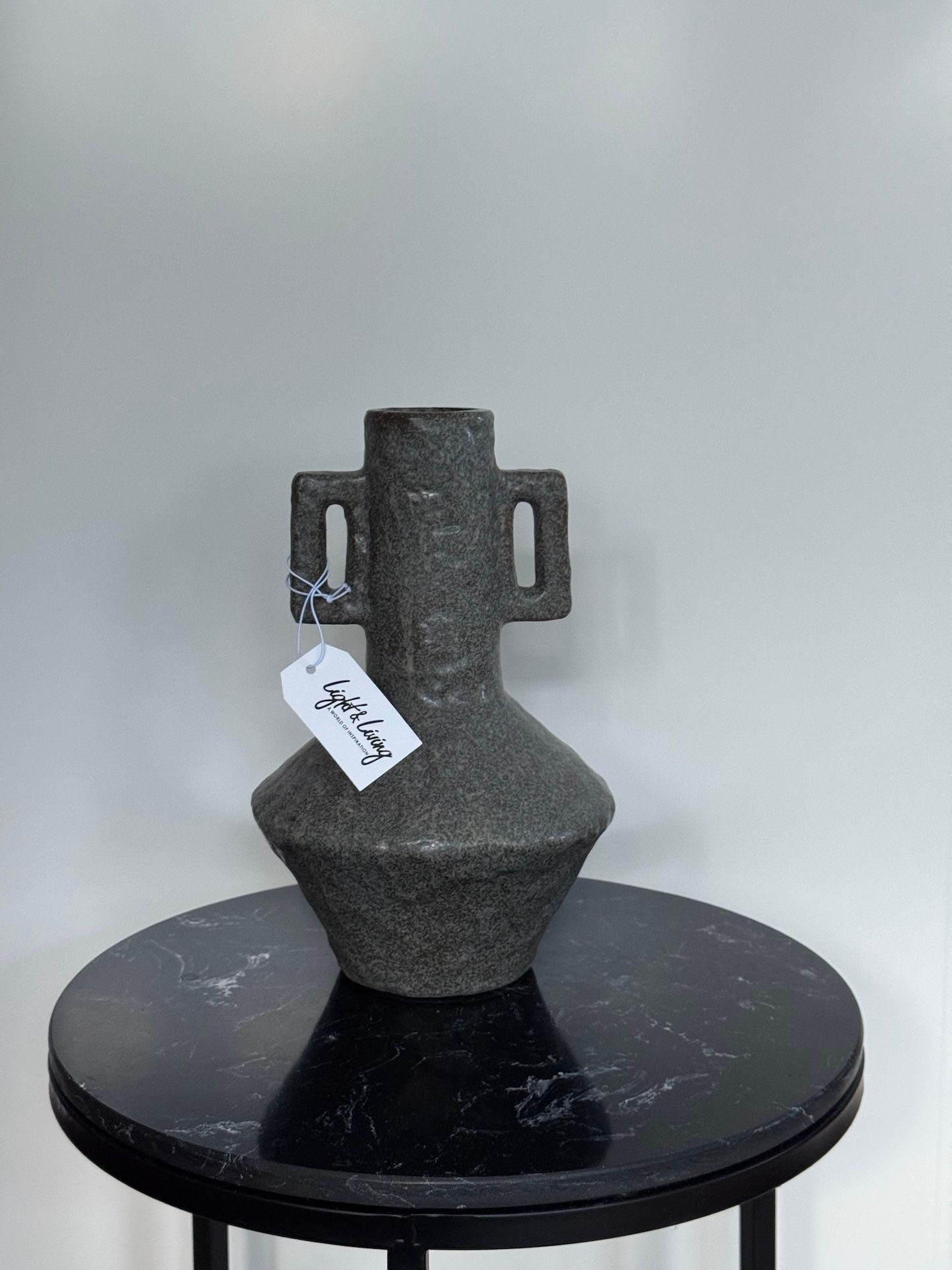 Donkere, gestructureerde vaas van keramiek met handvatten, staand op een zwart, gemarmerd oppervlak.