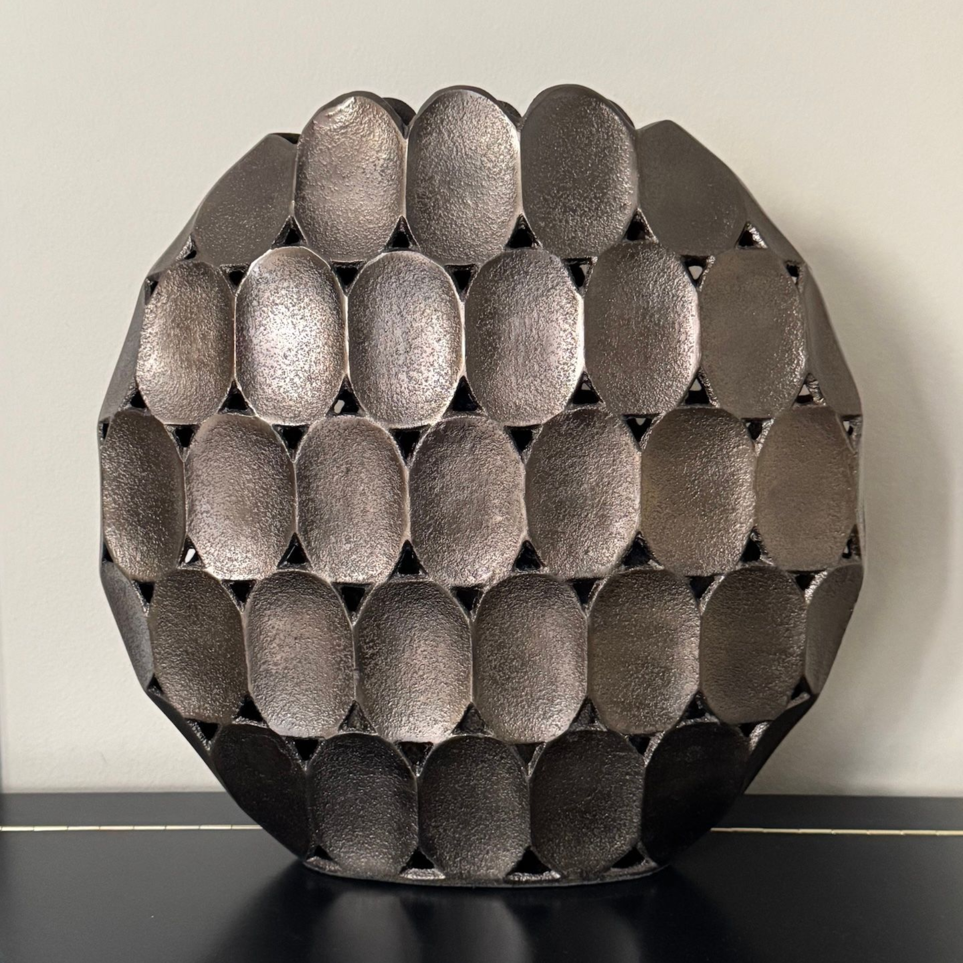 Decoratieve metalen bol met ovaal tegelontwerp, staand op een zwarte ondergrond.