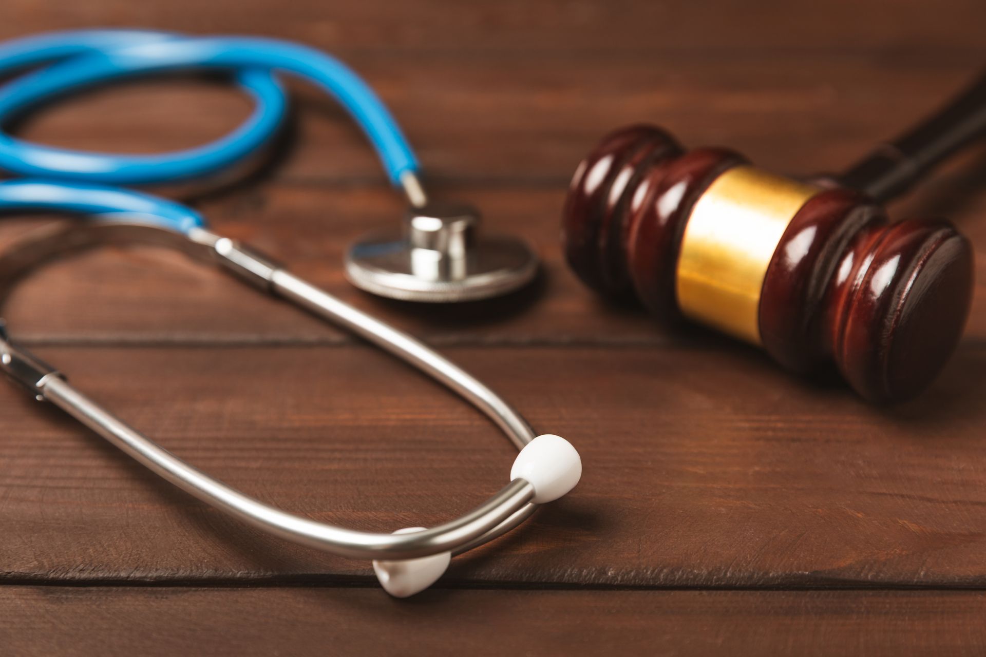 A blue stethoscope and a wooden judge's gavel placed on a dark wooden surface. A blue stethoscope and a wooden judge's gavel placed on a dark wooden surface.