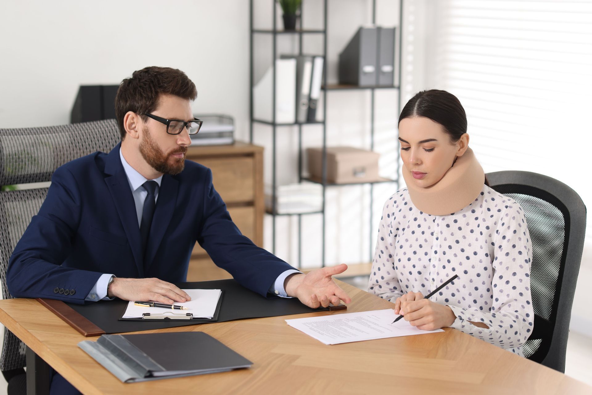 A woman wearing a neck brace & a man sit engaged in a conversation about personal injury attorneys.
