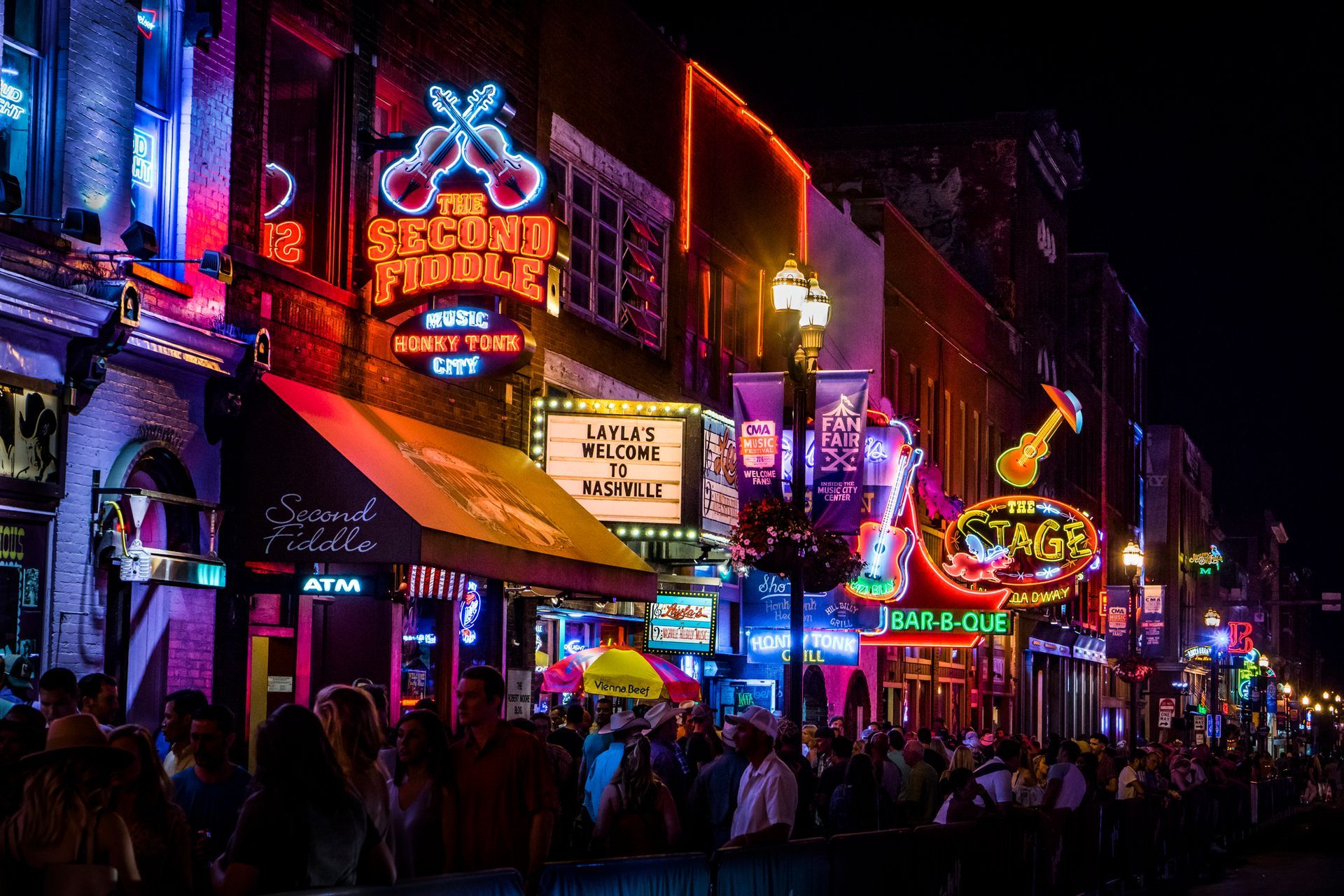 Neon-lit music venues and bars lining a nightlife street with crowds under colorful signs at night Neon-lit music venues and bars lining a nightlife street with crowds under colorful signs at night