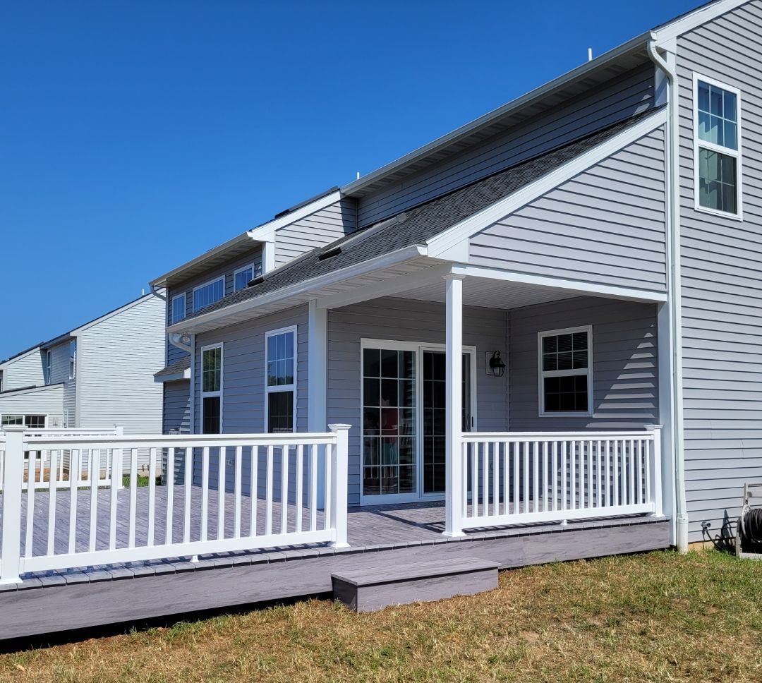A house with a gray deck and white railing. The deck leads to a covered patio with a sliding glass door and windows.